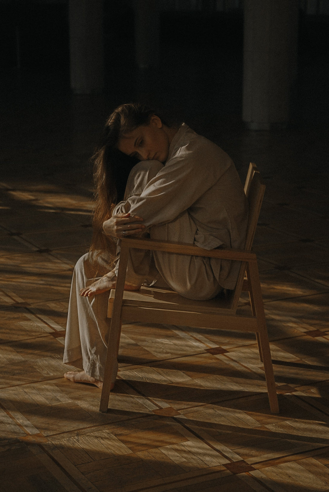 Photo of a woman sitting on a brown wooden chair. She looks sad, depressed and lonely. January Blues is often felt around the second week of January. Mental health awareness, self-care and wellbeing is important.